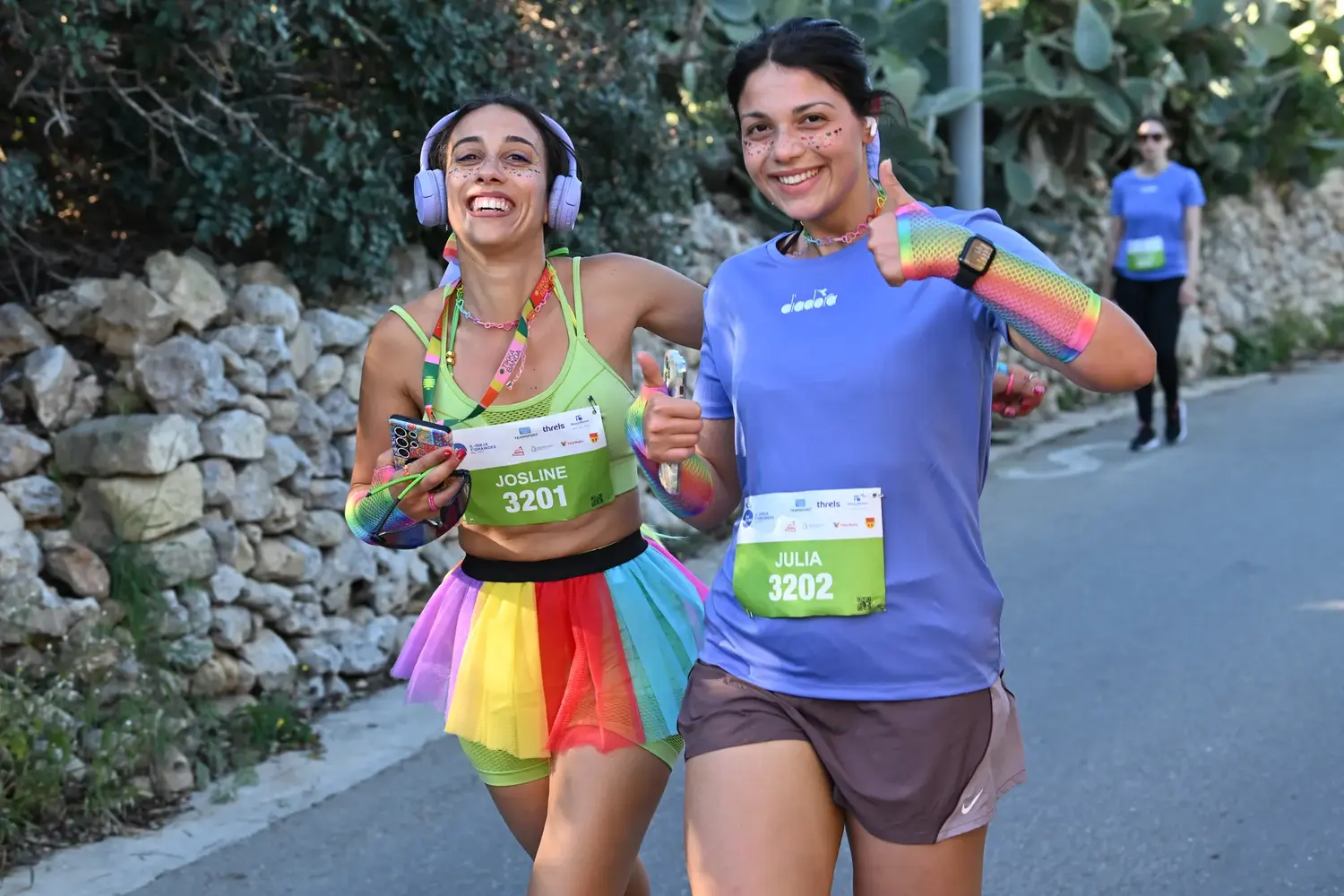 Two runners in rainbow tutus and face glitter giving a thumbs-up