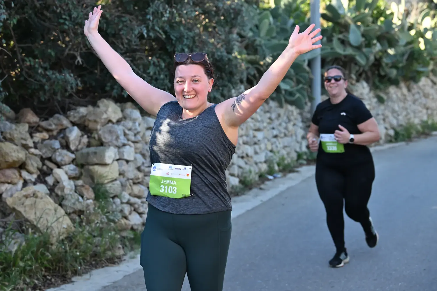 A runner throwing her arms in the air on a stone-walled road