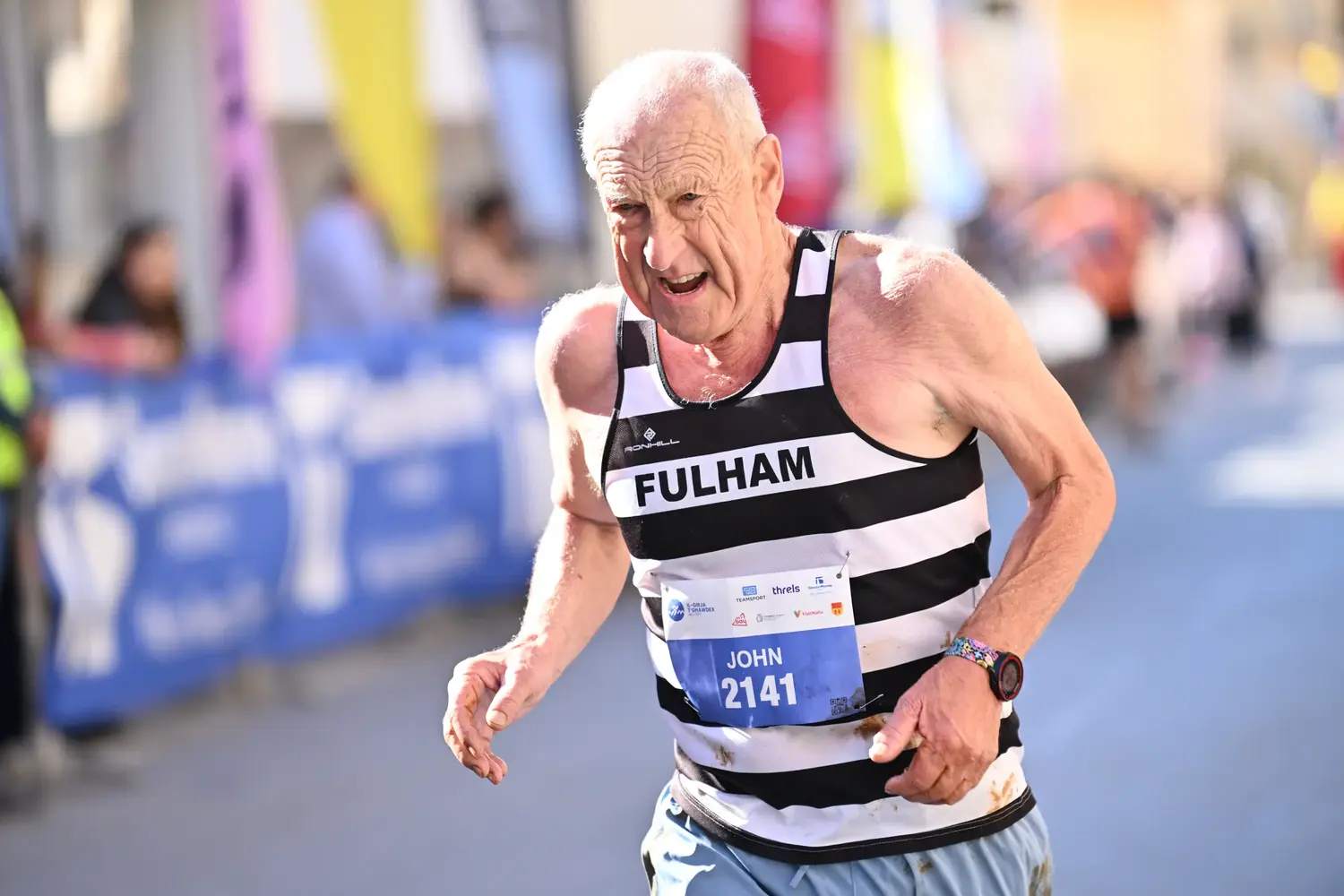 A veteran runner in a striped vest pushing on towards the finish