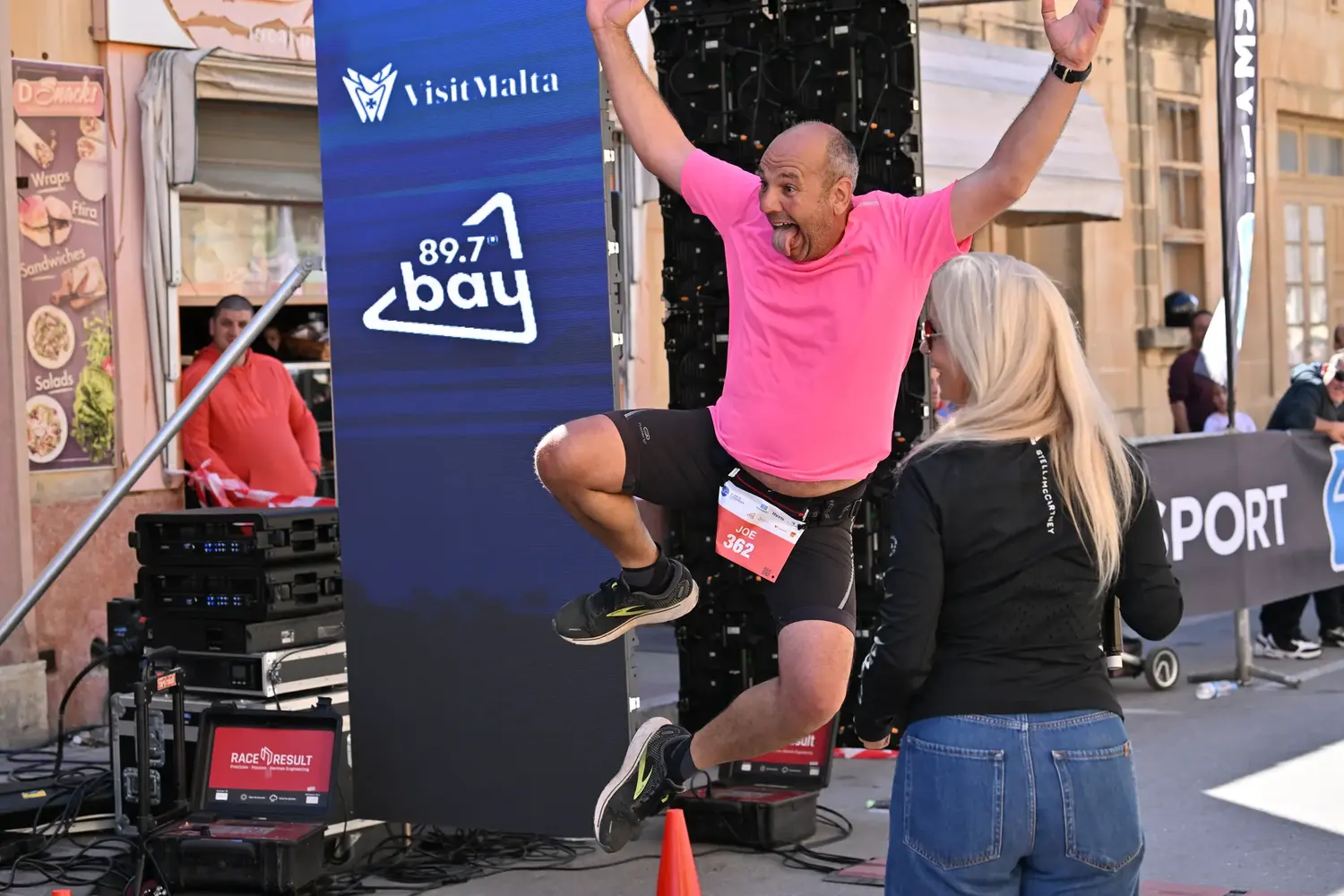 A runner in pink leaping for joy beside the music stage