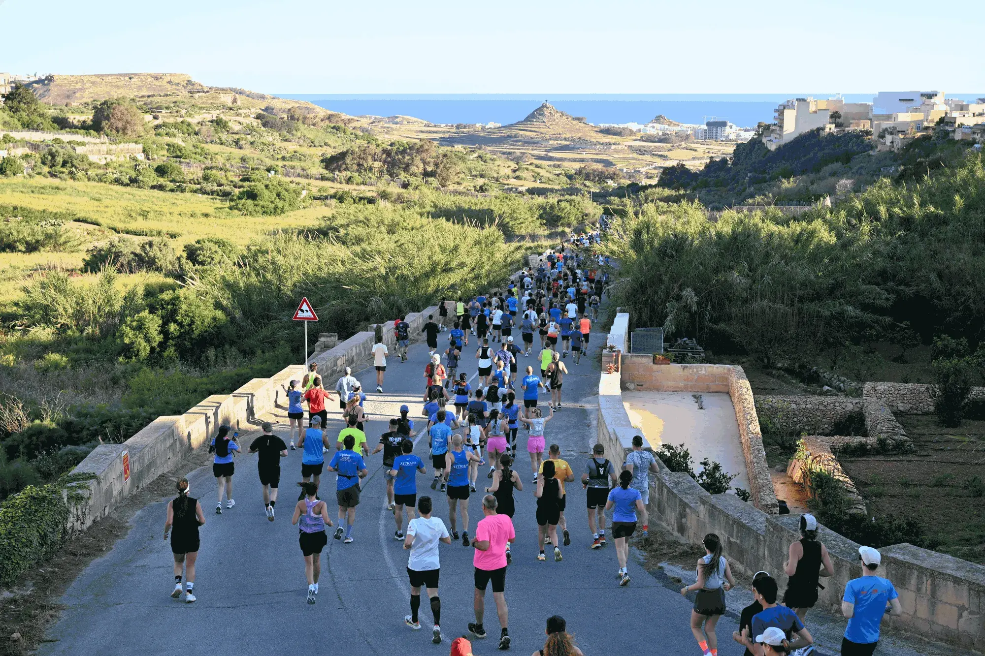 The field of il-Ġirja t'Għawdex running along a country road through the Gozitan countryside, with the sea on the horizon